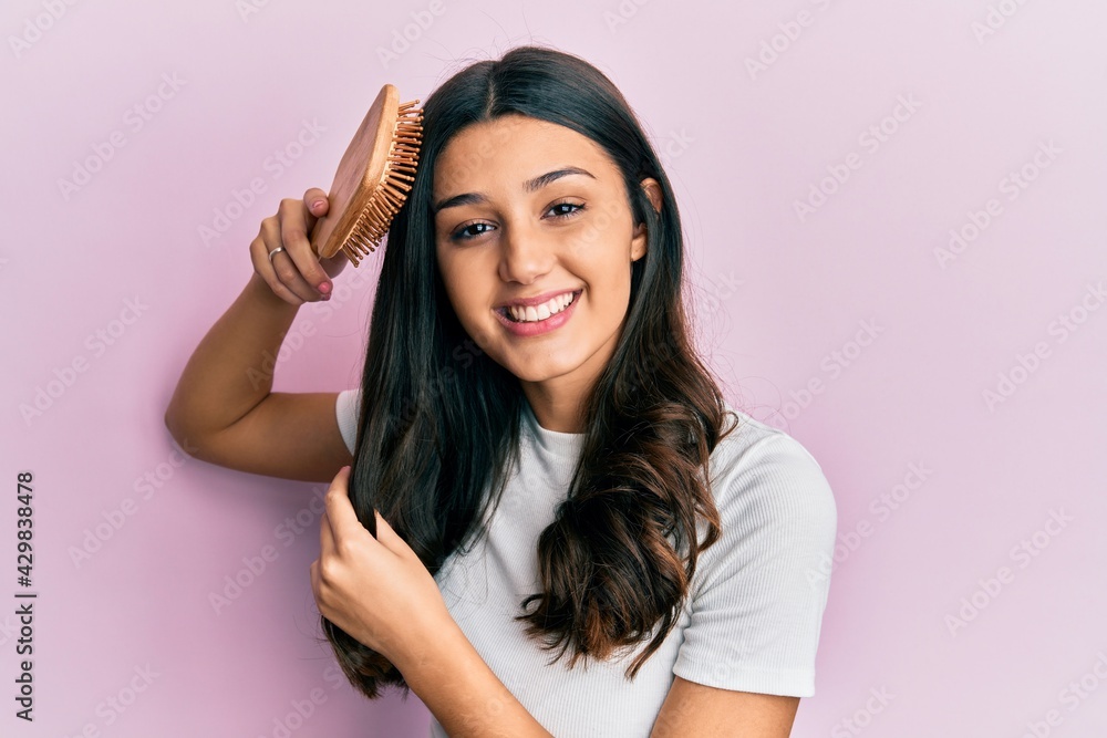Young hispanic woman styling hair using comb smiling with a happy and cool smile on face. showing teeth. - obrazy, fototapety, plakaty 