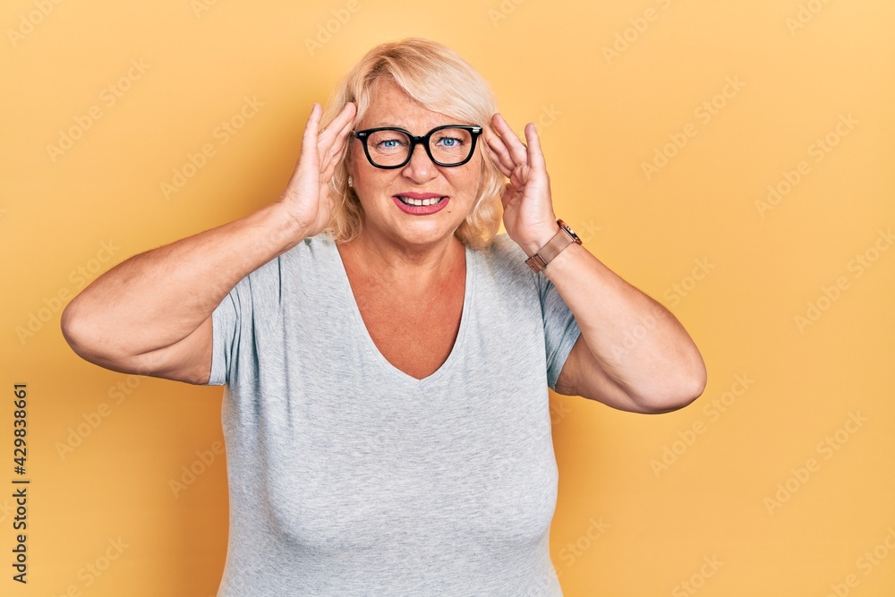 Middle age blonde woman wearing casual clothes and glasses suffering from headache desperate and stressed because pain and migraine. hands on head. Middle age blonde woman wearing casual clothes and glasses suffering from headache desperate and stressed because pain and migraine. hands on head.