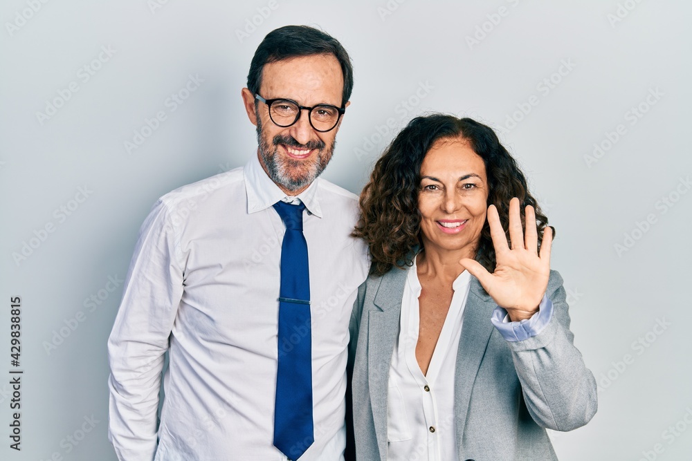 Middle age couple of hispanic woman and man wearing business office uniform showing and pointing up with fingers number five while smiling confident and happy. Middle age couple of hispanic woman and man wearing business office uniform showing and pointing up with fingers number five while smiling confident and happy.