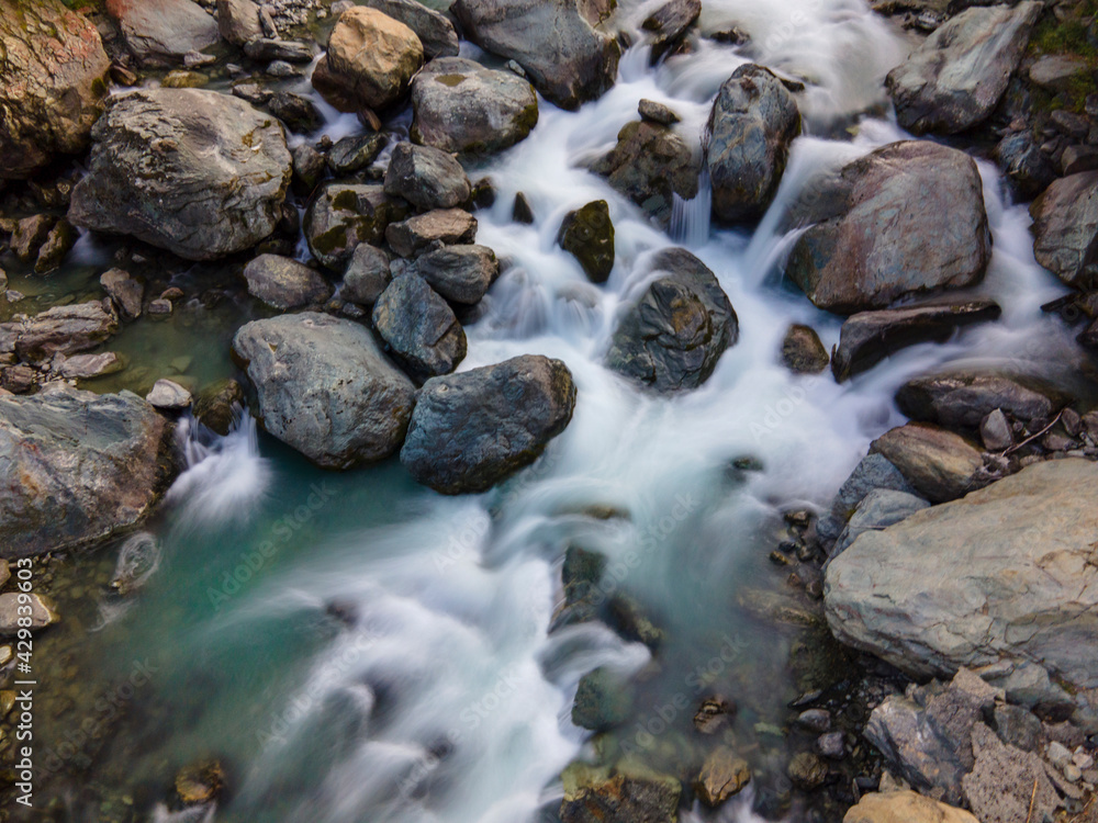 Aerial long exposure of alpine river in the mountain, silk effect, flowing water