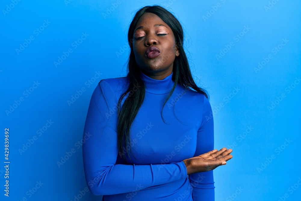African young woman presenting with open palm to the side looking at the camera blowing a kiss being lovely and sexy. love expression. African young woman presenting with open palm to the side looking at the camera blowing a kiss being lovely and sexy. love expression.