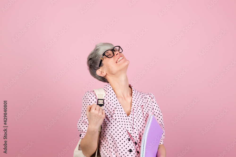 Stylish woman in dress and glasses on pink background with notebooks clenching fist winner gesture gesture education concept