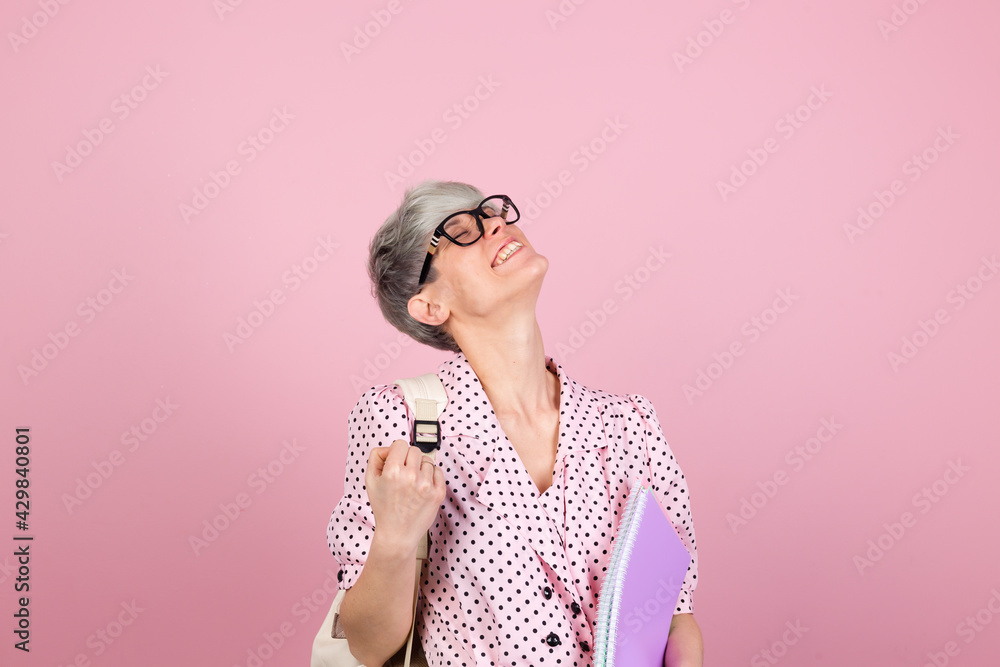 Stylish woman in dress and glasses on pink background with notebooks clenching fist winner gesture gesture education concept Stylish woman in dress and glasses on pink background with notebooks clenching fist winner gesture gesture education concept