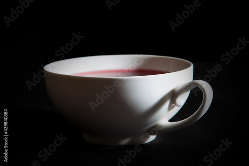 A white teacup with red berry tea. A black background