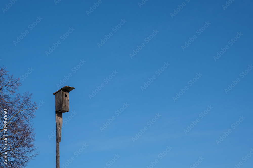 A wooden birdhouse on a tall thin pole against the blue sky. A wooden birdhouse on a tall thin pole against the blue sky.