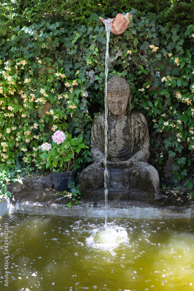 Pequeña fuente de jardín con estatua de buda entre árboles y arbustos