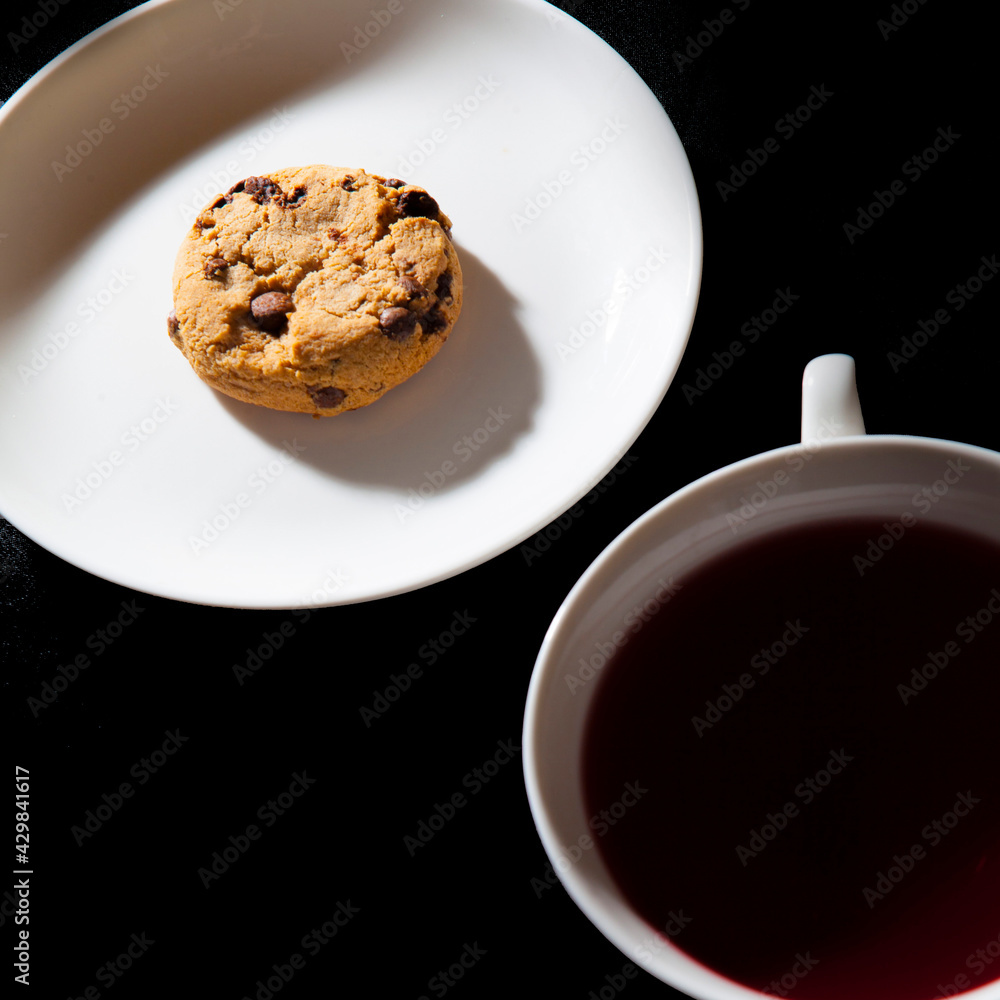 White cup of berry tea and cookie on the white plate. Black background White cup of berry tea and cookie on the white plate. Black background
