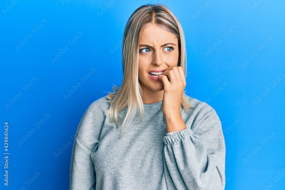 Beautiful blonde woman wearing casual clothes looking stressed and nervous with hands on mouth biting nails. anxiety problem. Beautiful blonde woman wearing casual clothes looking stressed and nervous with hands on mouth biting nails. anxiety problem.