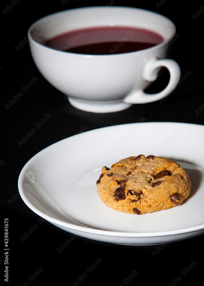 White cup of berry tea and cookie on the white plate. Black background