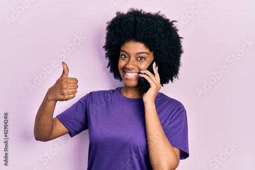 Young african american woman having conversation talking on the smartphone smiling happy and positive  thumb up doing excellent and approval sign