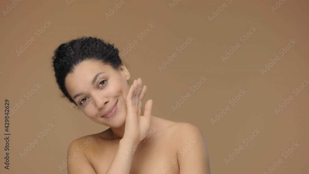 Beauty portrait of young African American woman, she gently touches face with her fingers. Black female model posing on brown studio background. Slow motion ready, 4K at 59.94fps. Beauty portrait of young African American woman, she gently touches face with her fingers. Black female model posing on brown studio background. Slow motion ready, 4K at 59.94fps.