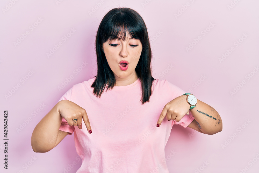 Young hispanic woman wearing casual clothes pointing down with fingers showing advertisement, surprised face and open mouth Young hispanic woman wearing casual clothes pointing down with fingers showing advertisement, surprised face and open mouth