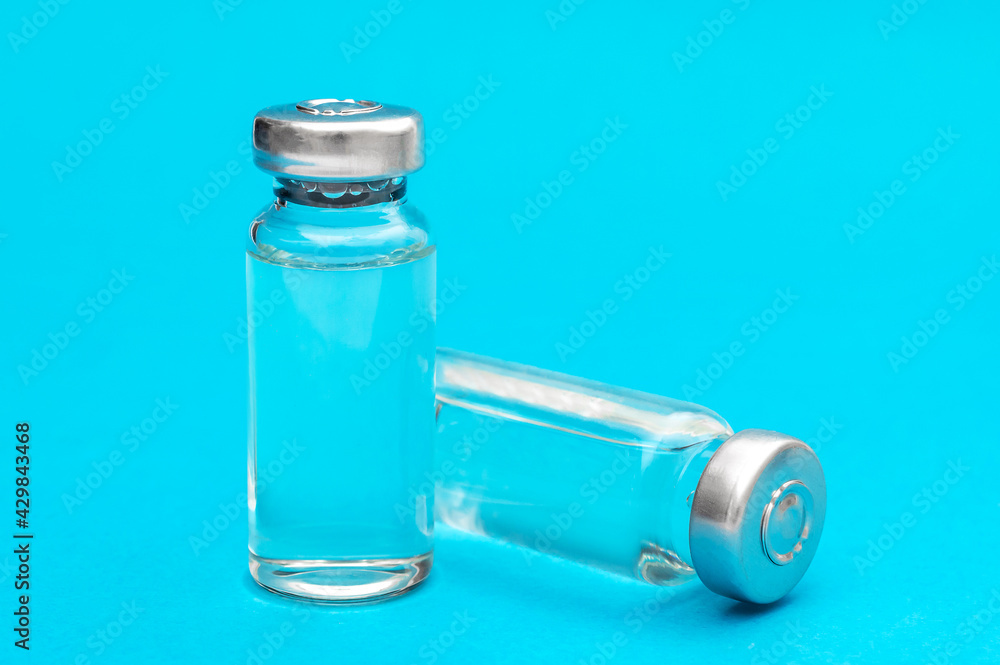 Two glass vials of vaccine on blue background. Close up. Two glass vials of vaccine on blue background. Close up.