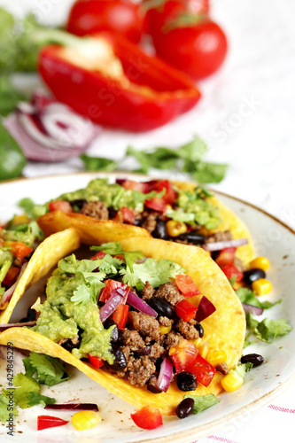 Mexican tacos with roast minced meat with corn and black beans, onions, fresh tomatoes, paprika and cilantro are flavored with guacamole sauce.