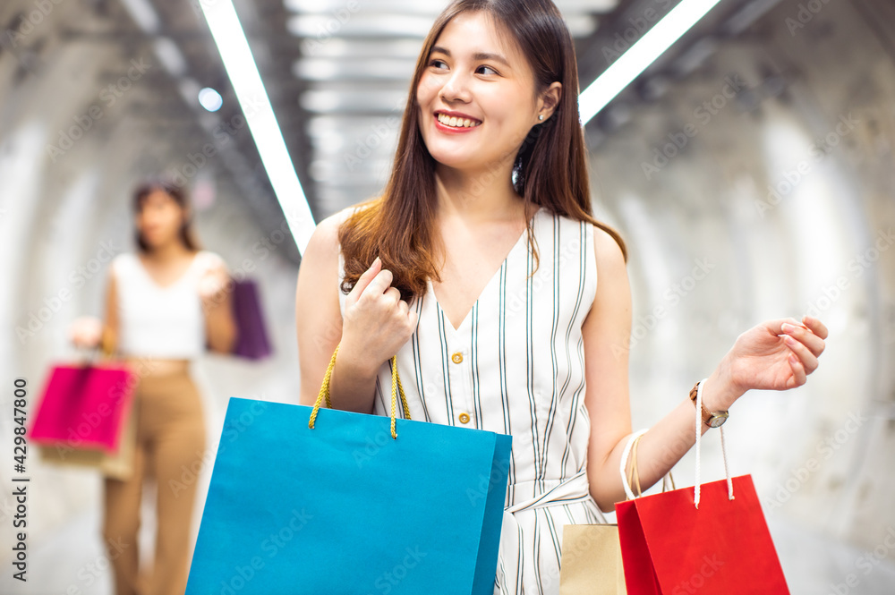 Asian woman wearing face mask. Happy woman with shopping bags enjoying in shopping. Girl holding colour paper bag.Friends walking in shopping mall.time shopping coronavirus crisis or covid19 outbreak Asian woman wearing face mask. Happy woman with shopping bags enjoying in shopping. Girl holding colour paper bag.Friends walking in shopping mall.time shopping coronavirus crisis or covid19 outbreak