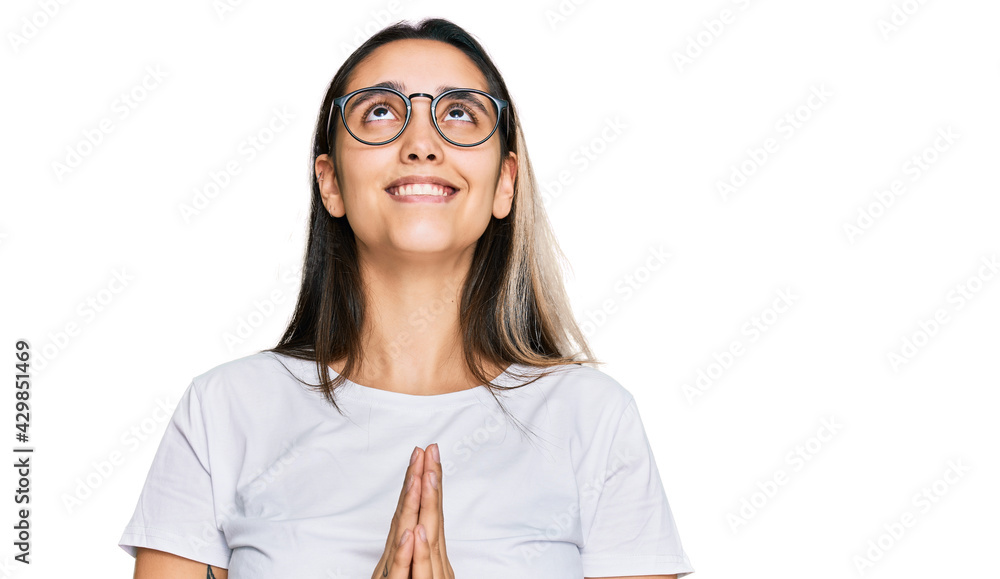 Young hispanic woman wearing casual white t shirt begging and praying with hands together with hope expression on face very emotional and worried. begging. Young hispanic woman wearing casual white t shirt begging and praying with hands together with hope expression on face very emotional and worried. begging.