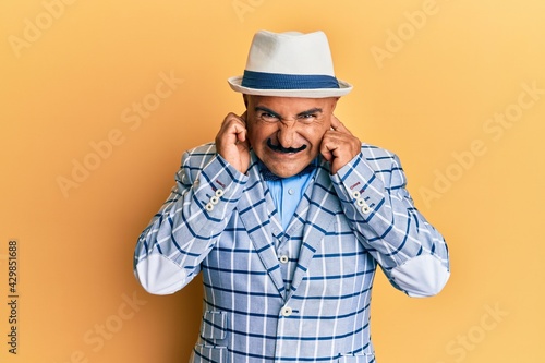 Mature middle east man with mustache wearing vintage and elegant fashion style covering ears with fingers with annoyed expression for the noise of loud music. deaf concept.