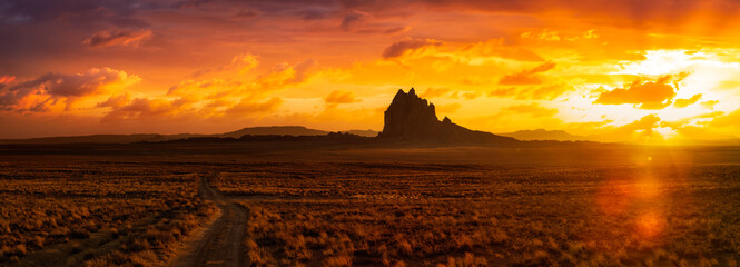 Leinwandbilder Honigfarbe Striking panoramic landscape view of a dirt road in the dry desert with a mountain peak in the background. Colorful Sunset Sky Art Render. Taken at Shiprock, New Mexico, United States.  © edb3_16