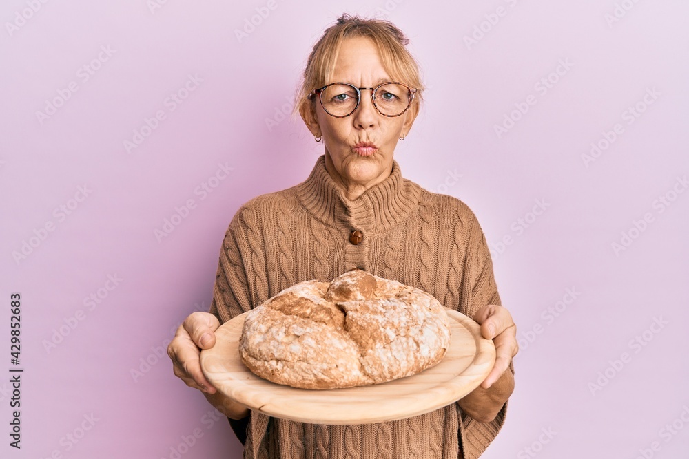 Middle age blonde woman holding bread looking at the camera blowing a kiss being lovely and sexy. love expression.