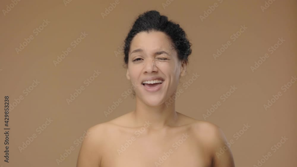 Beauty portrait of young African American woman smiles and winks coquettishly. Black female model posing on brown studio background. Slow motion ready, 4K at 59.94fps. Beauty portrait of young African American woman smiles and winks coquettishly. Black female model posing on brown studio background. Slow motion ready, 4K at 59.94fps.