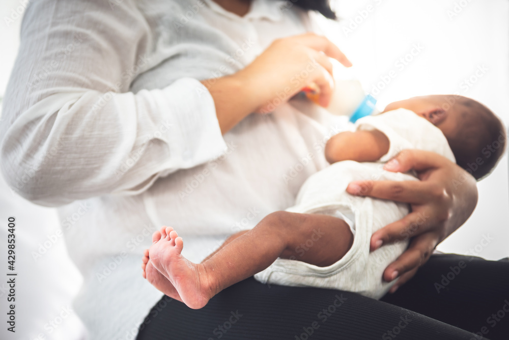 Blurred soft images of mother Sitting on bed, and feed milk from bottle milk to her 12-day-old African baby black skin newborn son, This picture focused on foot baby, to food for infant concept. Blurred soft images of mother Sitting on bed, and feed milk from bottle milk to her 12-day-old African baby black skin newborn son, This picture focused on foot baby, to food for infant concept.