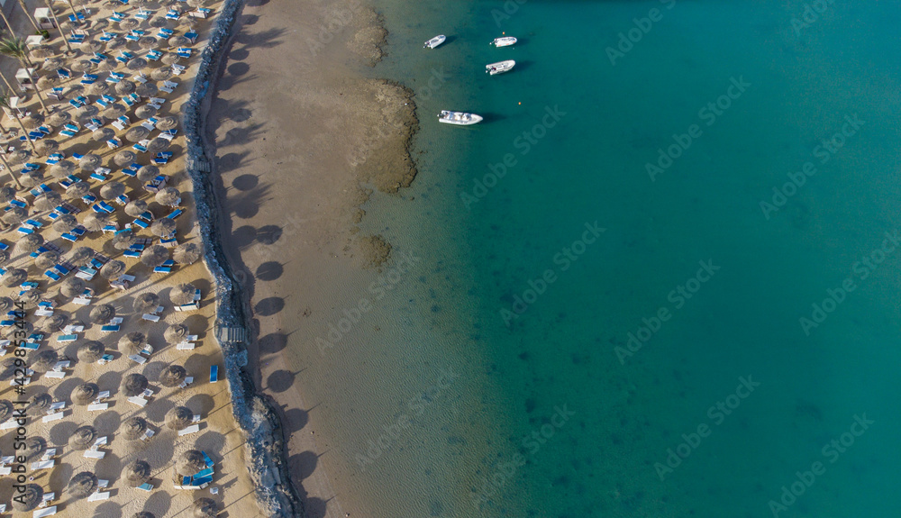 Top down view of a beach with tourists suntbeds and umbrellas with sand beach and clear blue water in egypt
