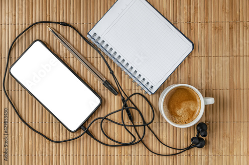 cup of coffee, smartphone, headphones, notepad and pen on a baboo straw surface, mock up, flat lay