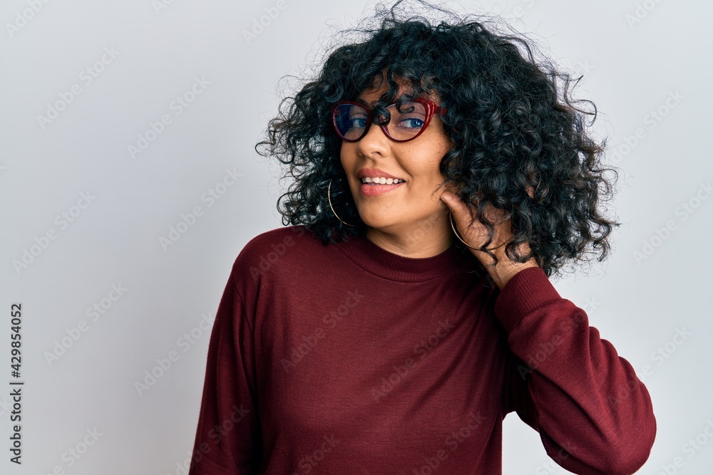 Young hispanic woman wearing casual clothes and glasses smiling with hand over ear listening and hearing to rumor or gossip. deafness concept. Young hispanic woman wearing casual clothes and glasses smiling with hand over ear listening and hearing to rumor or gossip. deafness concept.
