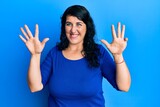 Plus size brunette woman wearing casual blue shirt showing and pointing up with fingers number nine while smiling confident and happy.