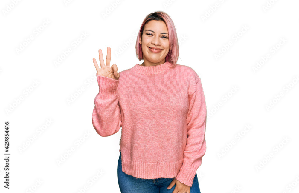 Hispanic woman with pink hair wearing casual winter sweater showing and pointing up with fingers number three while smiling confident and happy. Hispanic woman with pink hair wearing casual winter sweater showing and pointing up with fingers number three while smiling confident and happy.