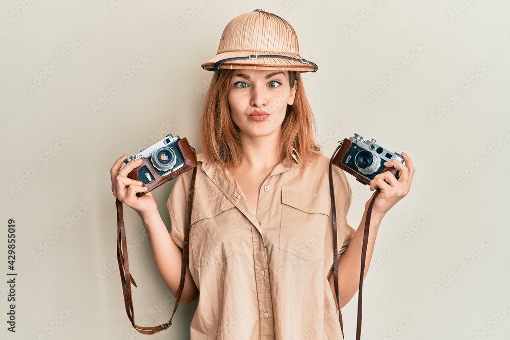 Young caucasian woman wearing explorer hat and vintage camera making fish  face with mouth and squinting eyes, crazy and comical. Stock Photo | Adobe  Stock