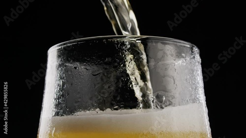 Beer pouring. Cold Beer in a glass with water drops. Fresh Beer into Glass on Black Background.