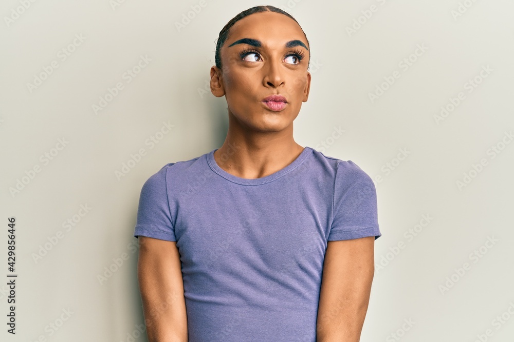 Hispanic man wearing make up and long hair wearing casual t shirt smiling looking to the side and staring away thinking. Hispanic man wearing make up and long hair wearing casual t shirt smiling looking to the side and staring away thinking.