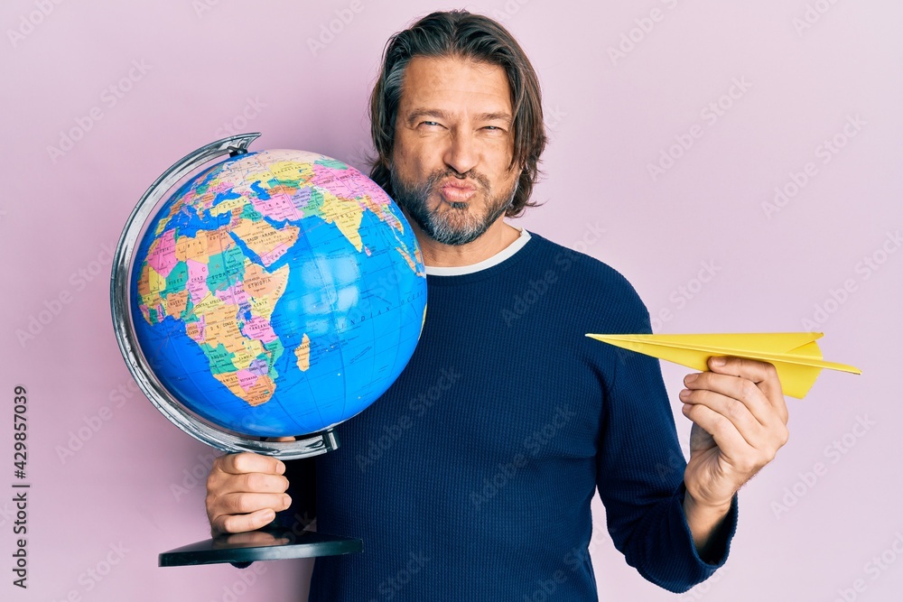 Fototapeta premium Middle age handsome man holding paper plane and world ball looking at the camera blowing a kiss being lovely and sexy. love expression.