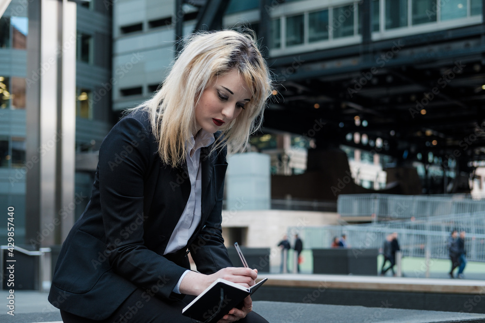 Fototapeta premium Atractive young business woman writing on a notepad. Outdoors.