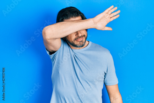 Middle age caucasian man wearing casual clothes covering eyes with arm, looking serious and sad. sightless, hiding and rejection concept