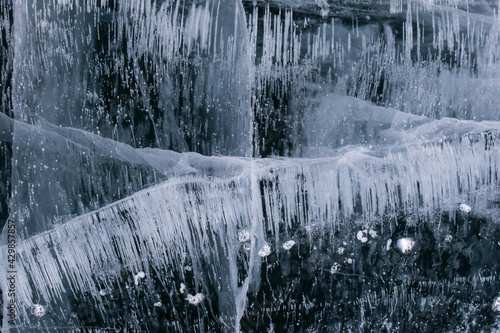 Frozen Baikal lake with cracks and methane bubbles on the transparent ice surface. Winter abstract and blue ice background.