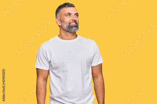Middle age handsome man wearing casual white tshirt looking away to side with smile on face, natural expression. laughing confident.