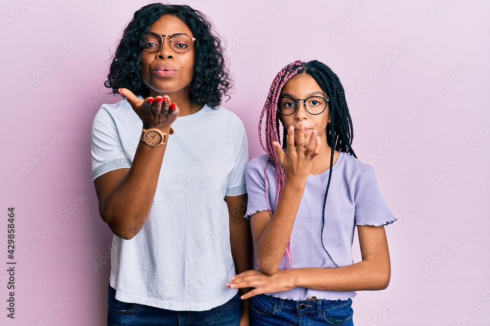 Beautiful african american mother and daughter wearing casual clothes and glasses looking at the camera blowing a kiss with hand on air being lovely and sexy. love expression. Beautiful african american mother and daughter wearing casual clothes and glasses looking at the camera blowing a kiss with hand on air being lovely and sexy. love expression.