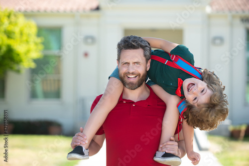 Fototapeta Naklejka Na Ścianę i Meble -  Father giving son piggyback ride after come back from school. School, family, education and outdoor concept. Funny kids face.
