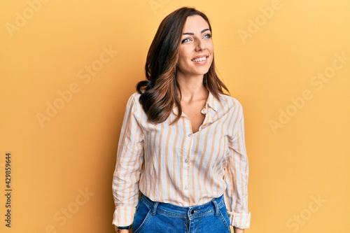 Young brunette woman wearing casual clothes over yellow background looking to side, relax profile pose with natural face and confident smile.