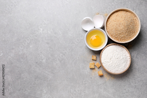 Fresh breadcrumbs, flour and egg on light grey table, flat lay. Space for text