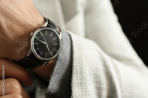 Businessman in jacket with luxury wrist watch on black background, closeup