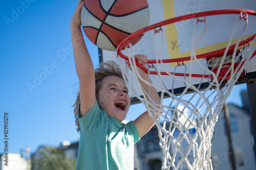 Closeup face of kid basketball player making slam dunk during basketball game. The child sport player, outdoor on basketball playground