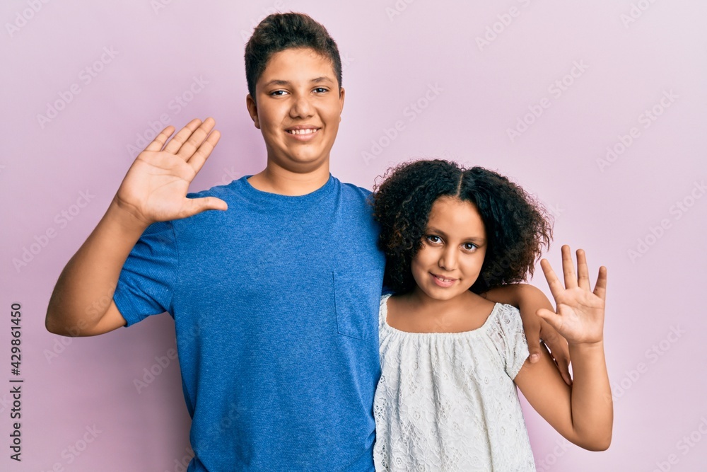 Obraz premium Young hispanic family of brother and sister wearing casual clothes together waiving saying hello happy and smiling, friendly welcome gesture