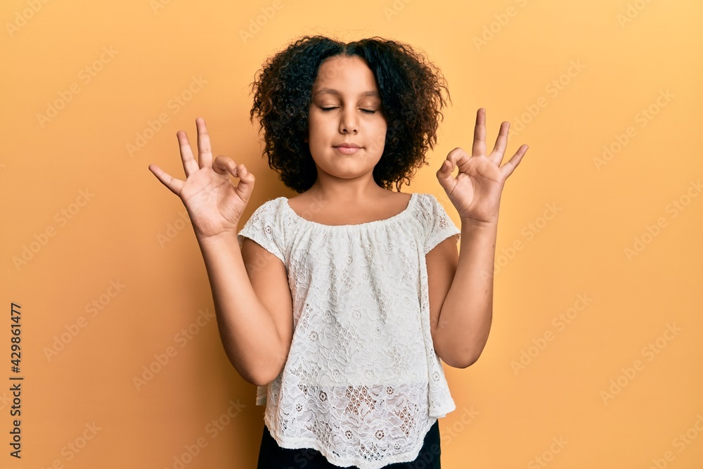 Young little girl with afro hair wearing casual clothes relax and smiling with eyes closed doing meditation gesture with fingers. yoga concept. Young little girl with afro hair wearing casual clothes relax and smiling with eyes closed doing meditation gesture with fingers. yoga concept.