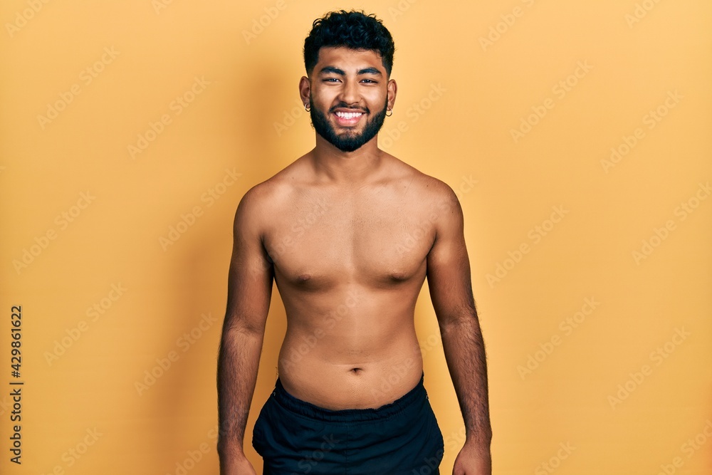 Arab man with beard wearing swimwear shirtless with a happy and cool smile on face. lucky person.
