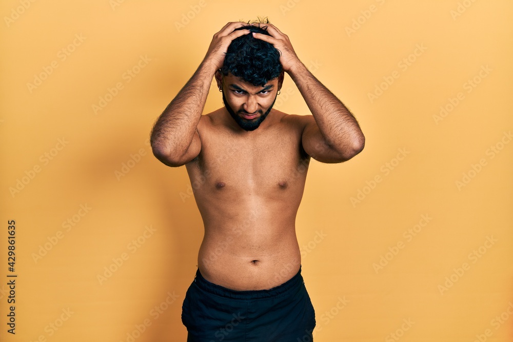 Arab man with beard wearing swimwear shirtless suffering from headache desperate and stressed because pain and migraine. hands on head.