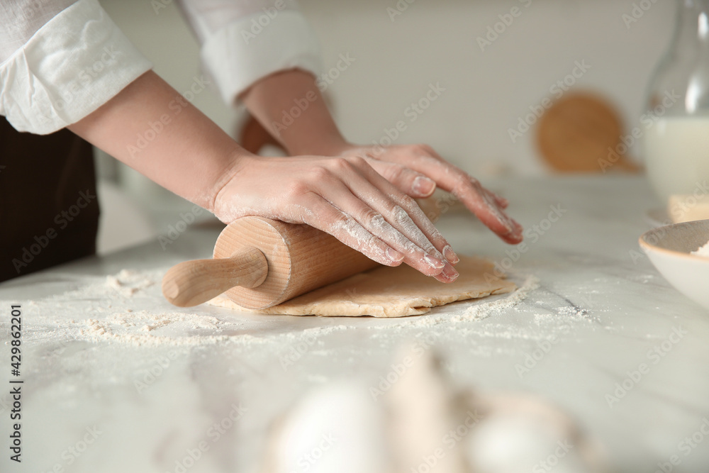 Woman rolling dough at table in kitchen, closeup