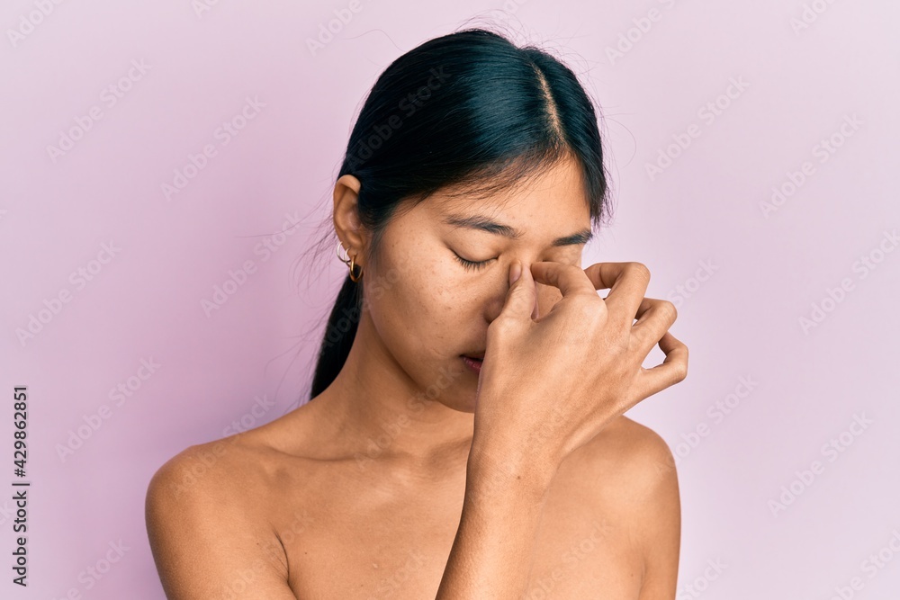 Young chinese woman standing topless showing skin tired rubbing nose and eyes feeling fatigue and headache. stress and frustration concept. Young chinese woman standing topless showing skin tired rubbing nose and eyes feeling fatigue and headache. stress and frustration concept.